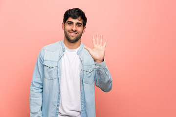 Young man over pink wall counting five with fingers