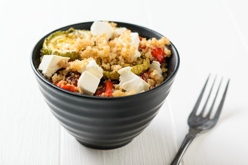 A fork next to a bowl of quinoa salad and baked vegetables on a white table. Vegetarian dish.