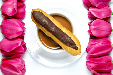 White coffee cup stands on a white plate with white background near multi-colored tulips