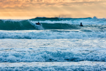 Fototapeta premium Sufers riding into colorful sunset at Piha Beach, New Zealand