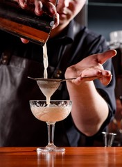 Barman makes a beautiful cocktail at the bar. The barman whipped the cocktail. Blurred bar. Space.