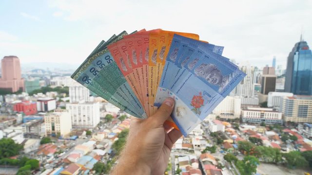 A young man holds in his hands the money of Malaysia against the background of the city center of Kuala Lumpur.