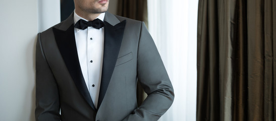Man model in expensive custom tailored tuxedo, suit standing and posing indoors