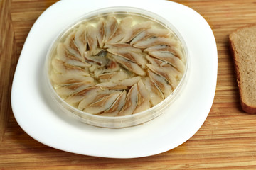 canned russian fish pieces of herring in oil in a jar on a white plate and wooden board  with bread