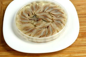 canned russian fish pieces of herring in oil in a jar on a white plate and wooden board  with bread