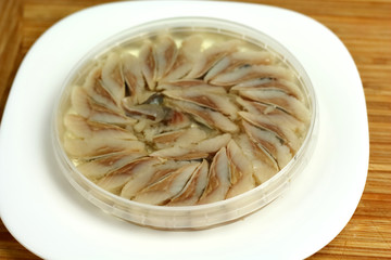 canned russian fish pieces of herring in oil in a jar on a white plate and wooden board  with bread
