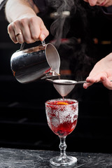 Bartender is making christmas mulled wine. Red mulled wine in a beautiful faceted glass with cranberries and orange slice. Dark background. close-up. space