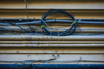 Wires - electrical, telephone, antenna, computer, network on the wall of a dilapidated house with peeling plaster, separate wires in metal pipes with protection