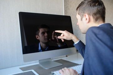 Obraz premium lateral view of a young man sitting in front of a computer and showing something with his finger on monitor