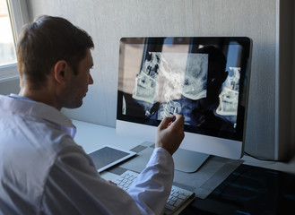 lateral view of a male radiologist examining neck x-rays (cervical vertebrae) on computer