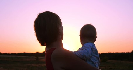 Cheery woman with a child in hands looking at splendid sunset outdoors in slo-mo