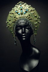 Black head of mannequin in decorated green kokoshnick, dark studio background