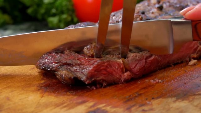 Mistress cuts the finished juicy beef steak on a wooden board with a large knife and fork