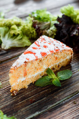 Slice of vegetable / carrot cake on a wooden background decorated with greens. Close-up. Space