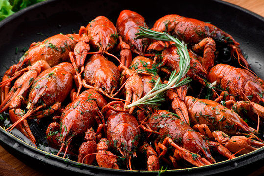 Beer Snack. Boiled crayfish in a cast-iron pan on a light wooden board on a dark wooden table. Close-up. Space
