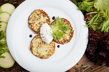 Lenten menu. Traditional Ukrainian, Russian and Belarusian dish - Draniki. Potato pancakes on a white plate with sour cream on a wooden background, decorated with vegetables. Rustic background
