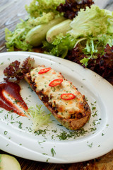 Baked stuffed zucchini with cheese and chilli on a white plate with red sauce. Wooden rustic background with vegetables and lettuce. Close-up. Space