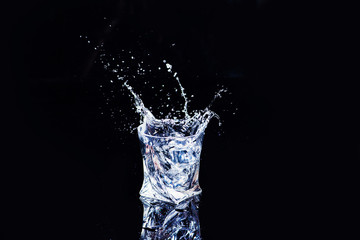 water in a glass with splash and cubes of ice on black background