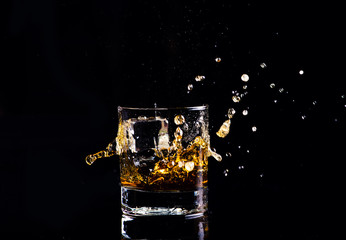 whiskey with splash on black background, brandy in a glass