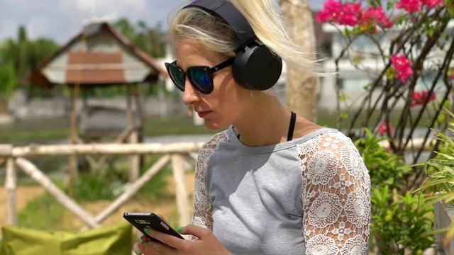 Young, happy woman listening to music on cellphone in garden cafe