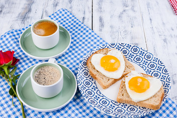 Two cups of aromatic coffee and heart-shaped toasts for a romantic morning of lovers. Red rose and morning surprise for breakfast. The concept of Valentine's Day and Mother's Day. Copy space. 