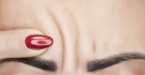 A woman shows deep wrinkles on her forehead. Aging process and cosmological skin care.