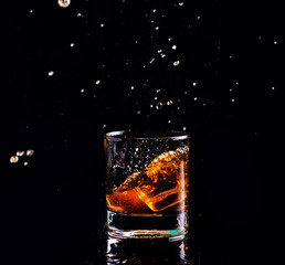 whiskey with splash on black background, brandy in a glass