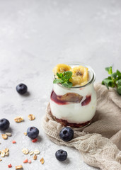 Granola, blueberry and banana greek yogurt parfaits in mason jars. Healthy breakfast. A light grey concrete background. Copy space.