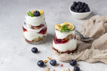 Granola, blueberry and banana greek yogurt parfaits in mason jars. Healthy breakfast. A light grey concrete background. Copy space.