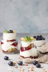 Granola, blueberry and banana greek yogurt parfaits in mason jars. Healthy breakfast. A light grey concrete background. Copy space.