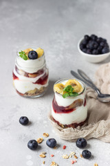 Granola, blueberry and banana greek yogurt parfaits in mason jars. Healthy breakfast. A light grey concrete background. Copy space.