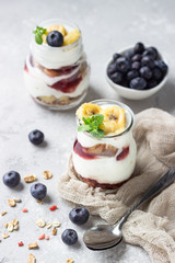 Granola, blueberry and banana greek yogurt parfaits in mason jars. Healthy breakfast. A light grey concrete background. Copy space.