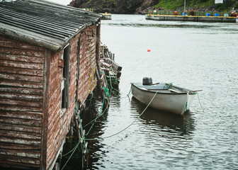 Fototapeta na wymiar Small fishing boat tied up to a fishing shed in a safe harbor along the coast of Newfoundland, Canada.