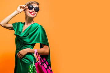 Elegant shopping woman with shopping bags wearing bright green dress ansd sunglasses