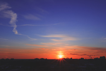 Naklejka na ściany i meble Beautiful sunset over the city. Sun rays shining from behind buildings