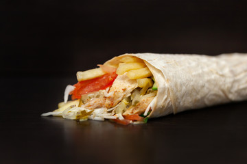 Shawarma sandwich - fresh roll of thin lavash (pita bread) filled with grilled meat, mushrooms, cheese, cabbage, carrots, sauce, green. Traditional Eastern snack. On a wooden background