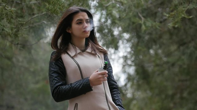 beautiful young girl vaping e-cigarette in the forest,closeup