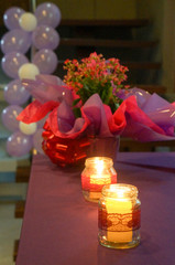 table with candles and flowers, party balloons in the background                            