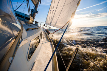 White yacht sailing at sunset. A view from the deck to the bow and sails. Waves and clouds. Baltic...