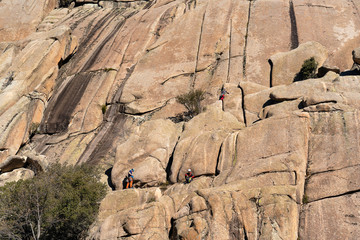 Climbers in a huge granite cliff rock in La Pedriza, National Park of mountain range of Guadarrama in Manzanares El Real, Madrid, Spain.