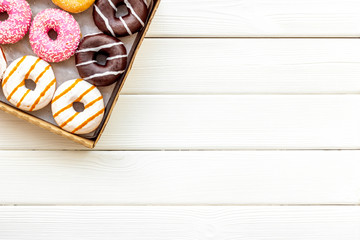 Glazed decorated donuts in box on white wooden background flat lay mock up