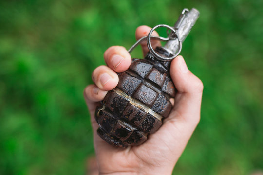 Closeup top view of white kid hand holding real old grenade. Horizontal color photography.
