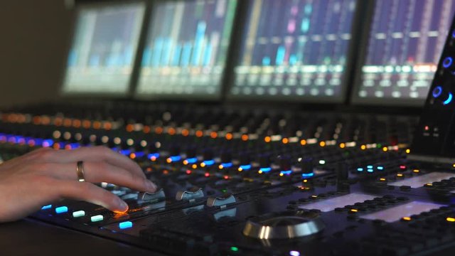 A man works in a recording studio on a mixing console. Hands close up