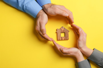 Couple holding hands near figure of house on color background, top view with space for text. Home...