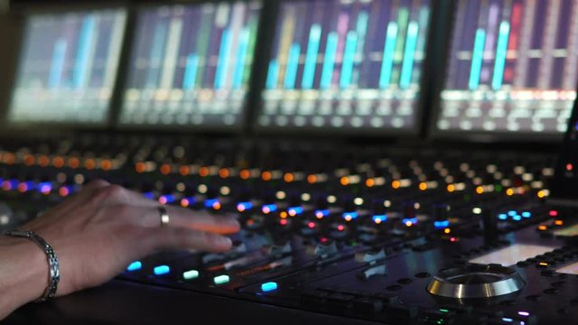 A man works in a recording studio on a mixing console. Hands close up