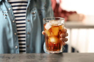 Woman holding glass of cola with ice at table, closeup