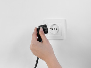 Woman putting plug into power socket on white background, closeup. Electrician's equipment