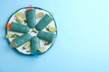 Plate with spirulina popsicles, mint and lime slices on color background, top view. Space for text