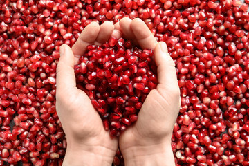 Woman holding pomegranate seeds over grains, top view