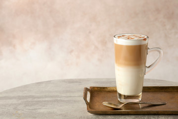 Tray with glass cup of caramel macchiato and syrup on table against color background. Space for text